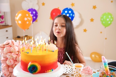 Photo of Cute little girl blowing out candles on her birthday cake indoors