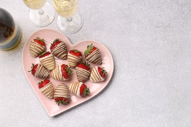 Photo of Heart shaped plate with delicious chocolate covered strawberries and sparkling wine on light table, flat lay. Space for text