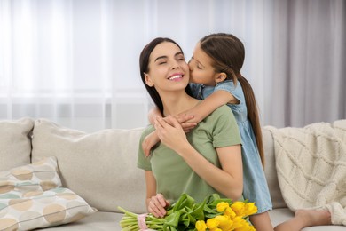 Photo of Happy woman with her daughter and bouquet of yellow tulips on sofa at home, space for text. Mother's day celebration