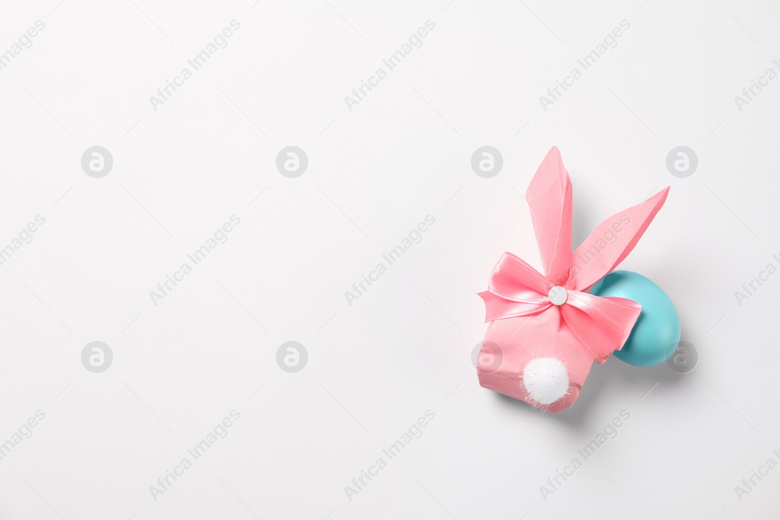 Photo of Easter bunny gift bag and dyed egg on white background, top view