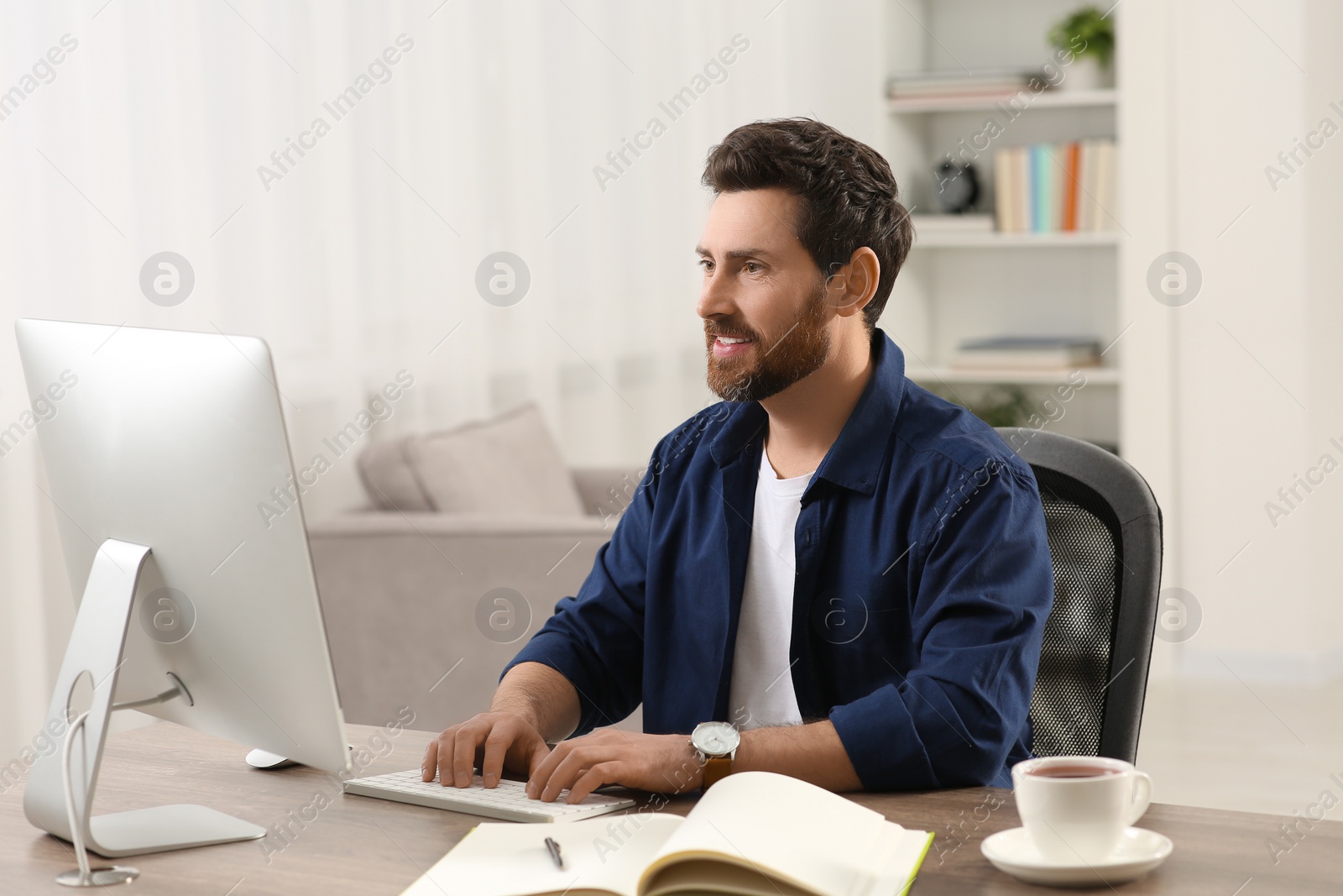 Photo of Home workplace. Happy man working with computer at wooden desk in room