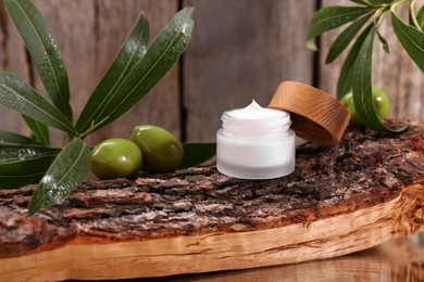 Photo of Glass jar of cream, olives and leaves on log near wooden wall