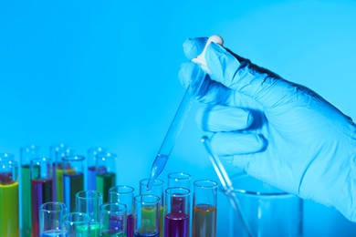 Photo of Scientist dripping liquid from pipette into test tube on light blue background, closeup