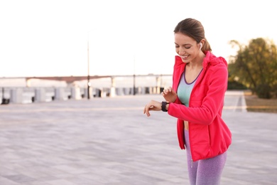 Photo of Young woman with wireless headphones and smartwatch listening to music outdoors. Space for text