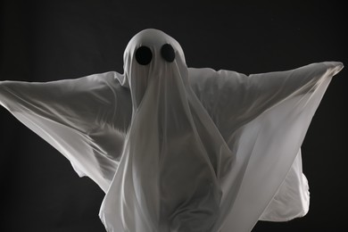 Photo of Creepy ghost. Person covered with white sheet on black background