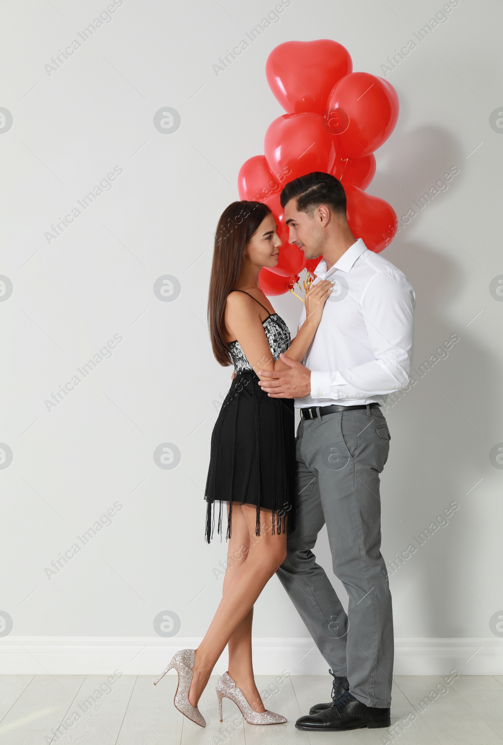 Photo of Beautiful couple with heart shaped balloons near light wall