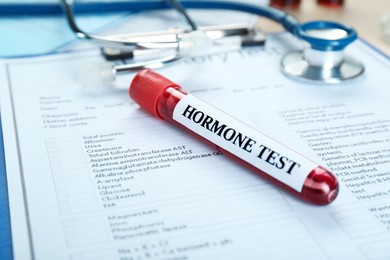 Photo of Hormone test. Sample tube with blood and stethoscope on laboratory forms, closeup