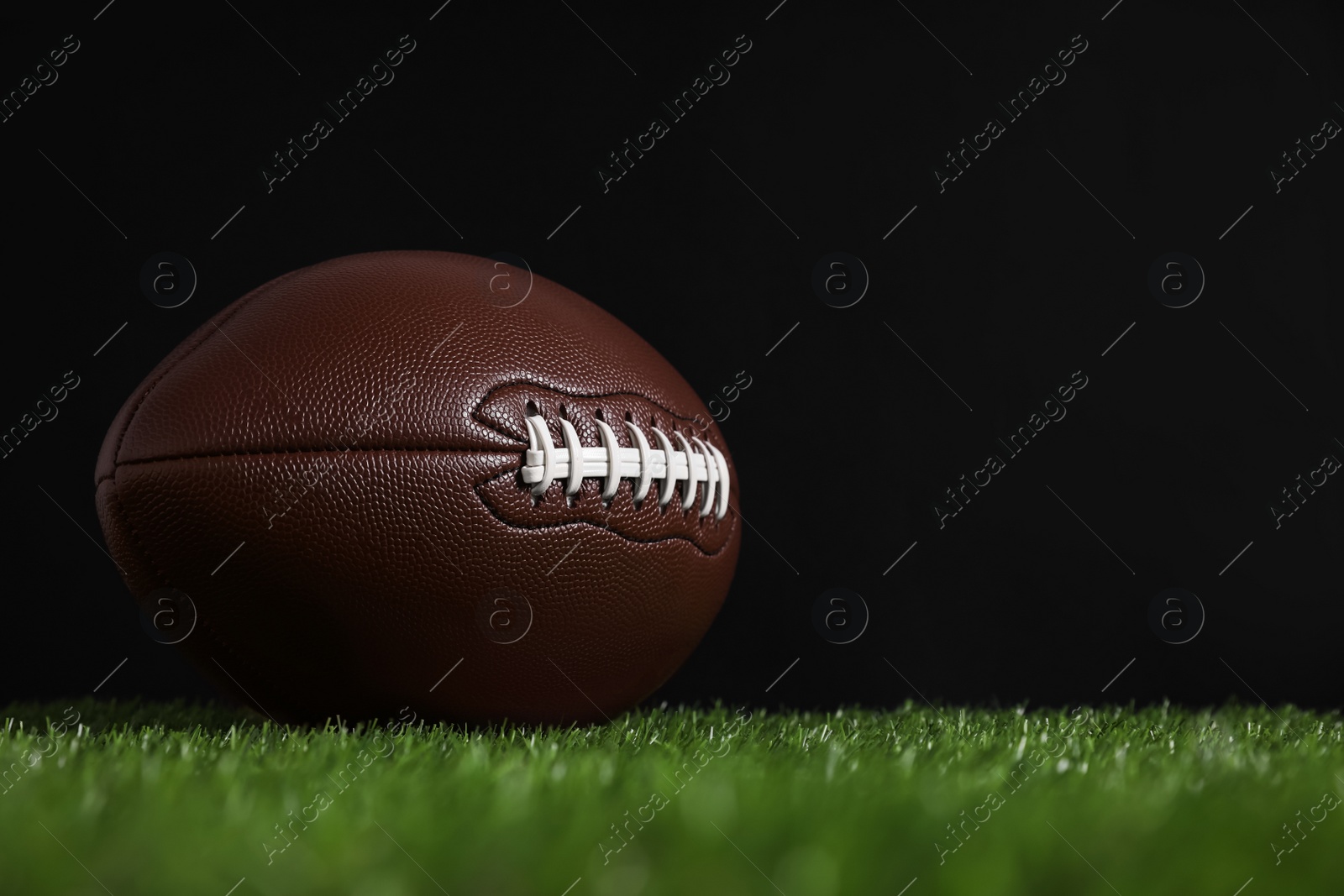 Photo of American football ball on green grass against black background. Space for text