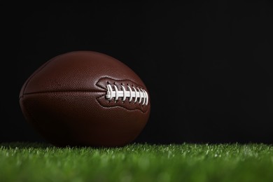 American football ball on green grass against black background. Space for text