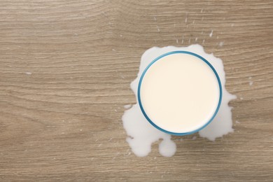 Photo of Spilled milk and glass of drink on wooden table, top view. Space for text