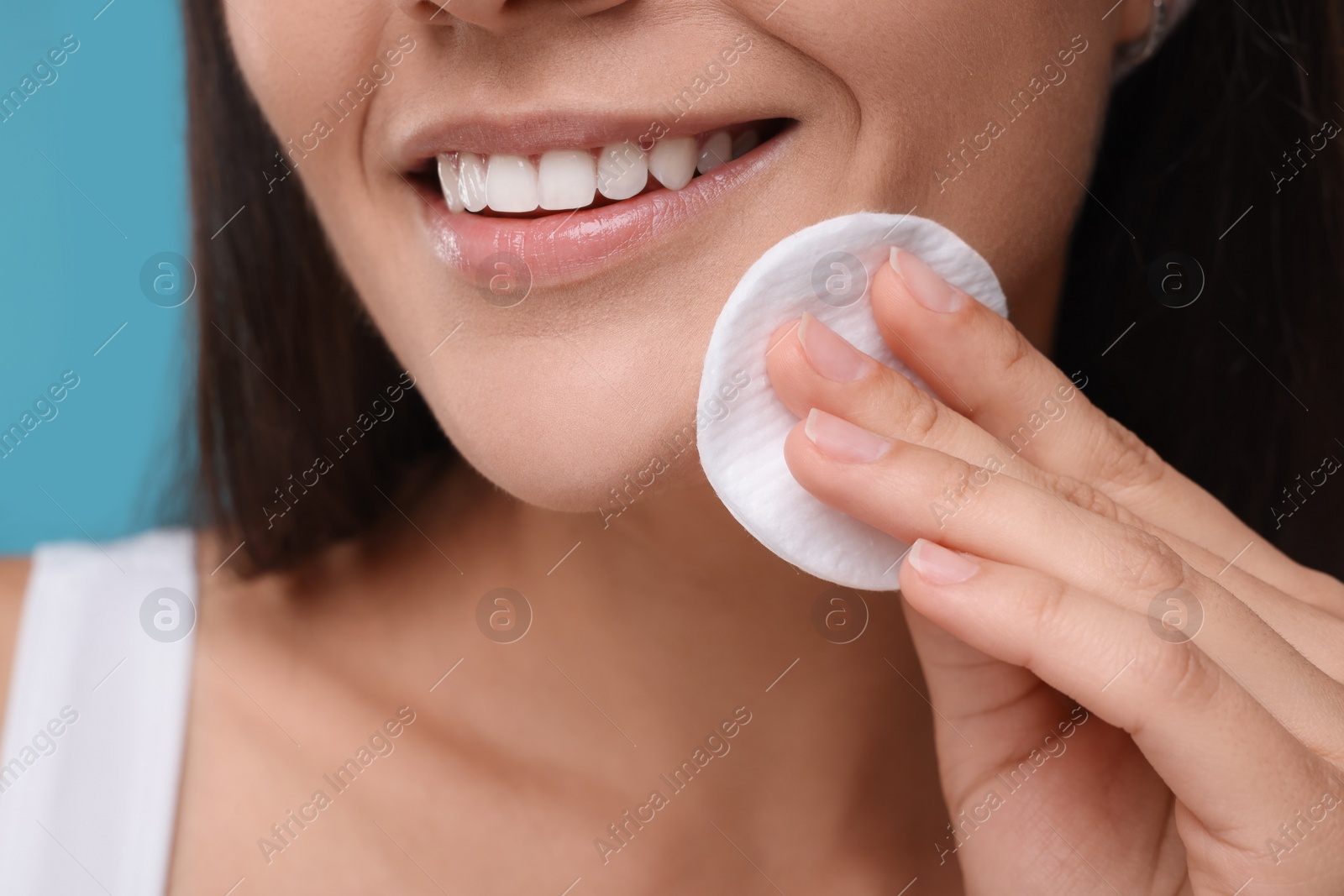 Photo of Young woman with cotton pad on light blue background, closeup