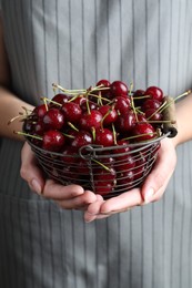 Photo of Woman holding metal basket with sweet juicy cherries, closeup