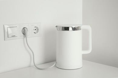 Electric kettle plugged into power socket on white wall