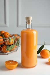 Photo of Bottle with tasty tangerine liqueur and fresh citrus fruit on white table