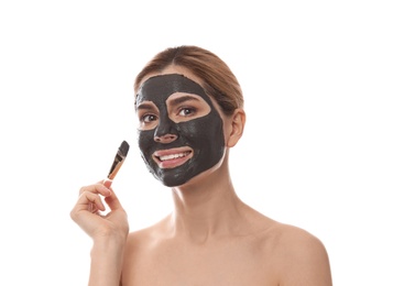 Photo of Beautiful woman applying black mask onto face against white background