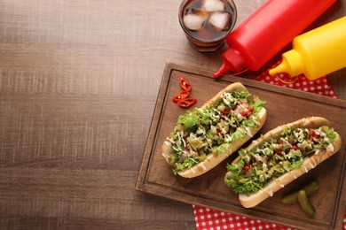 Photo of Tasty hot dogs with chili, lettuce, pickles and sauces served on wooden table, flat lay. Space for text