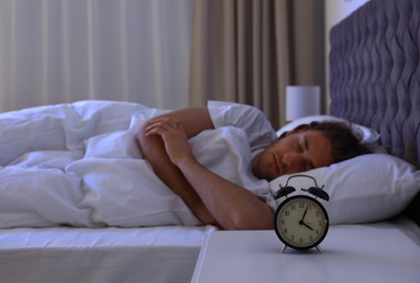 Photo of Alarm clock on nightstand near sleeping young man. Bedtime