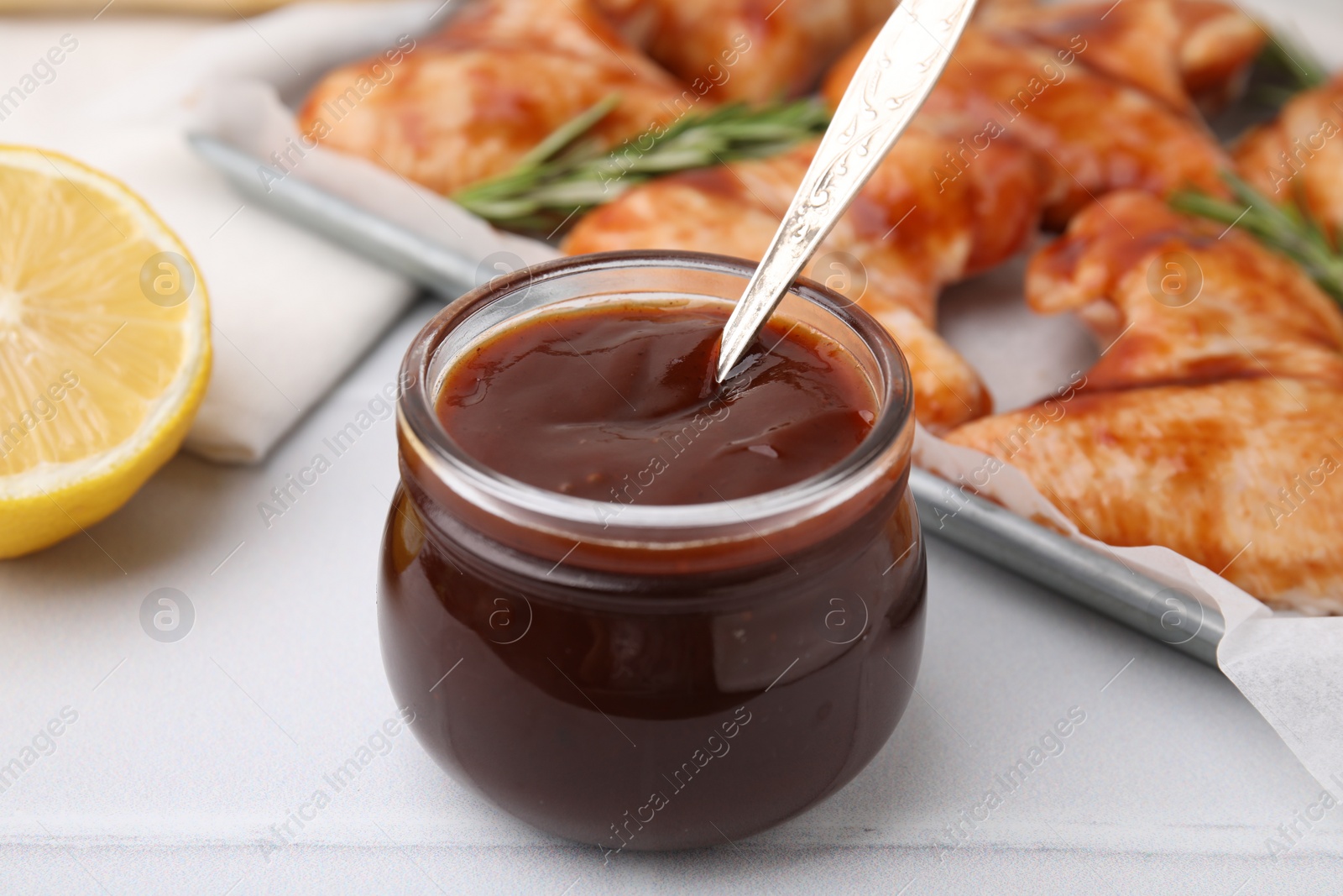 Photo of Fresh marinade with spoon in jar on light tiled table, closeup