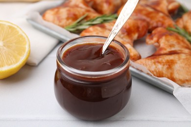 Fresh marinade with spoon in jar on light tiled table, closeup