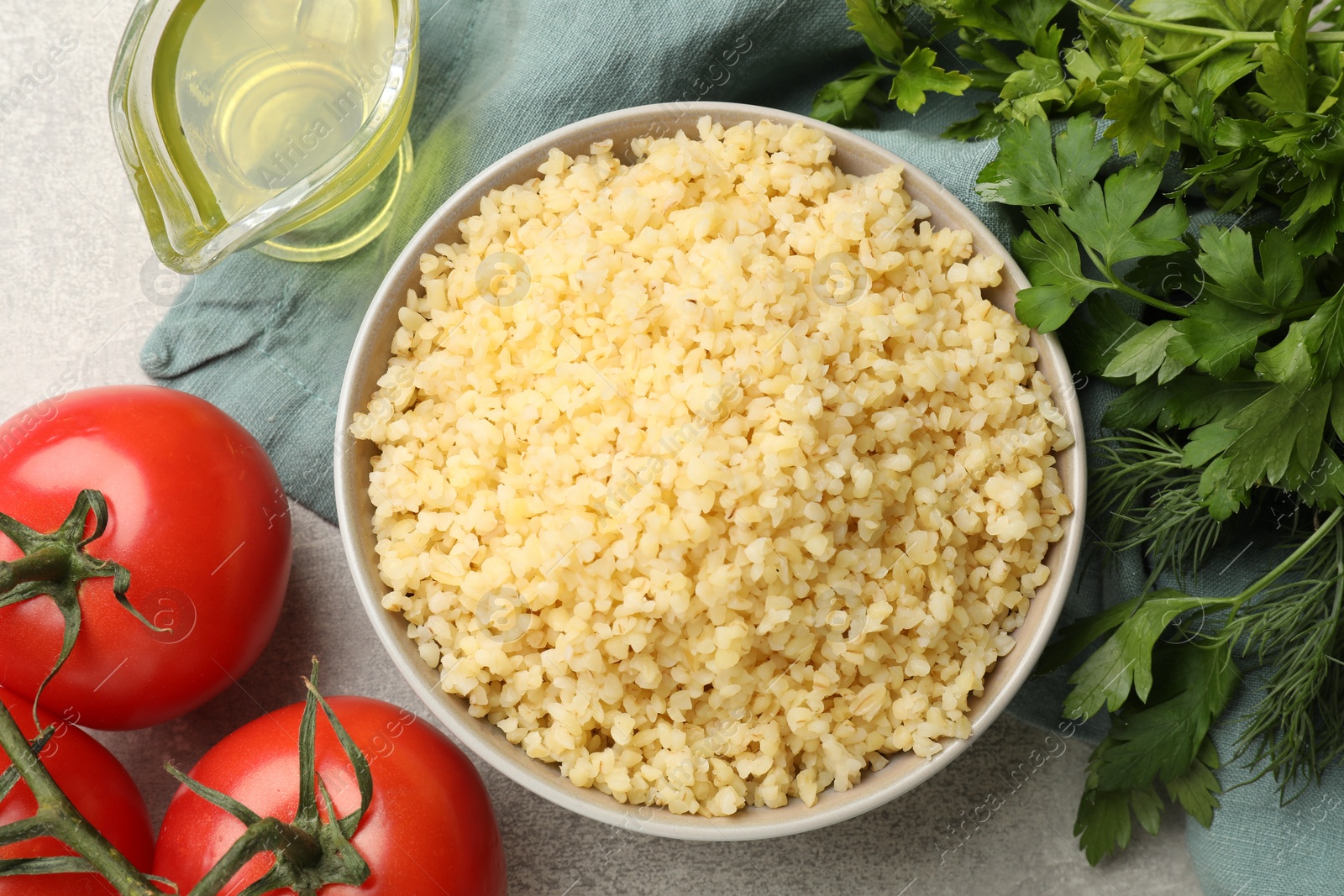 Photo of Delicious bulgur in bowl, tomatoes, greens and oil on table, flat lay