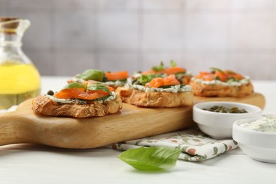 Tasty canapes with salmon, capers and sauce on white wooden table