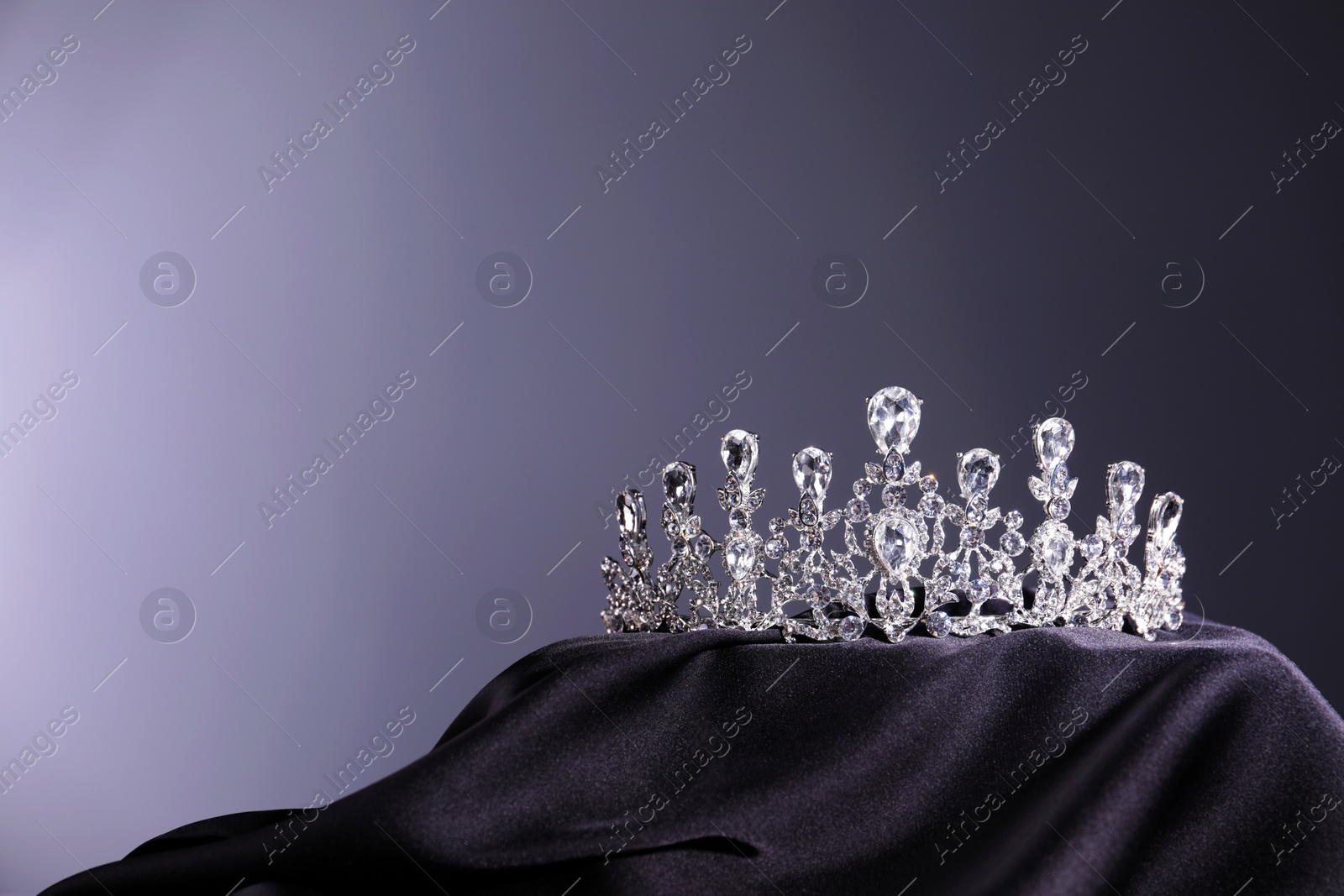 Photo of Beautiful silver tiara with diamonds on dark cloth against grey background. Space for text