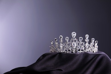 Beautiful silver tiara with diamonds on dark cloth against grey background. Space for text