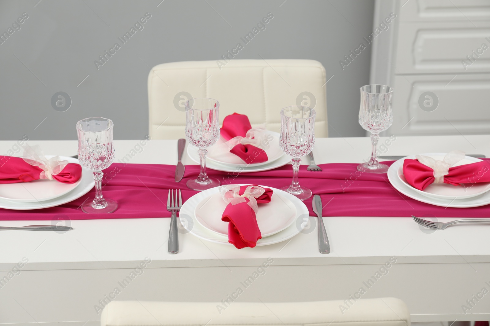 Photo of Color accent table setting. Glasses, plates, cutlery and pink napkins in dining room