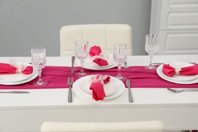 Color accent table setting. Glasses, plates, cutlery and pink napkins in dining room