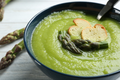 Delicious asparagus soup in bowl on white wooden table, closeup