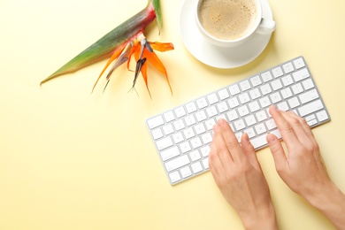 Photo of Woman using computer keyboard on table decorated with tropical flower, top view. Creative design ideas