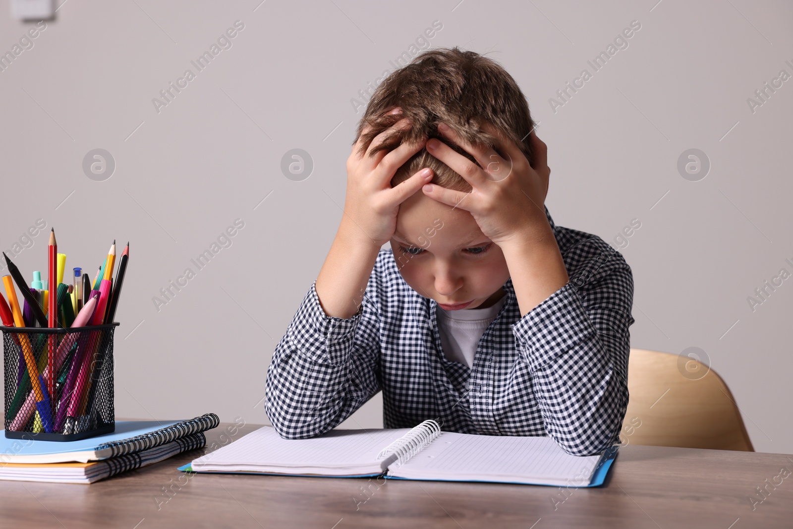 Photo of Little boy with stationery suffering from dyslexia at wooden table