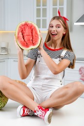Photo of Beautiful teenage girl with half of watermelon on table in kitchen