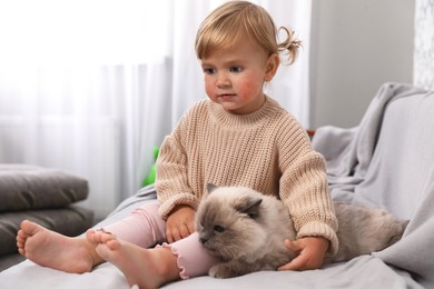 Cute little child with allergic redness sitting with adorable pet on sofa at home