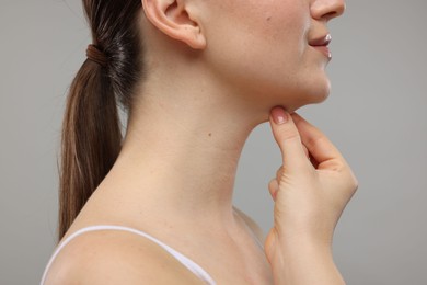 Woman touching her chin on grey background, closeup