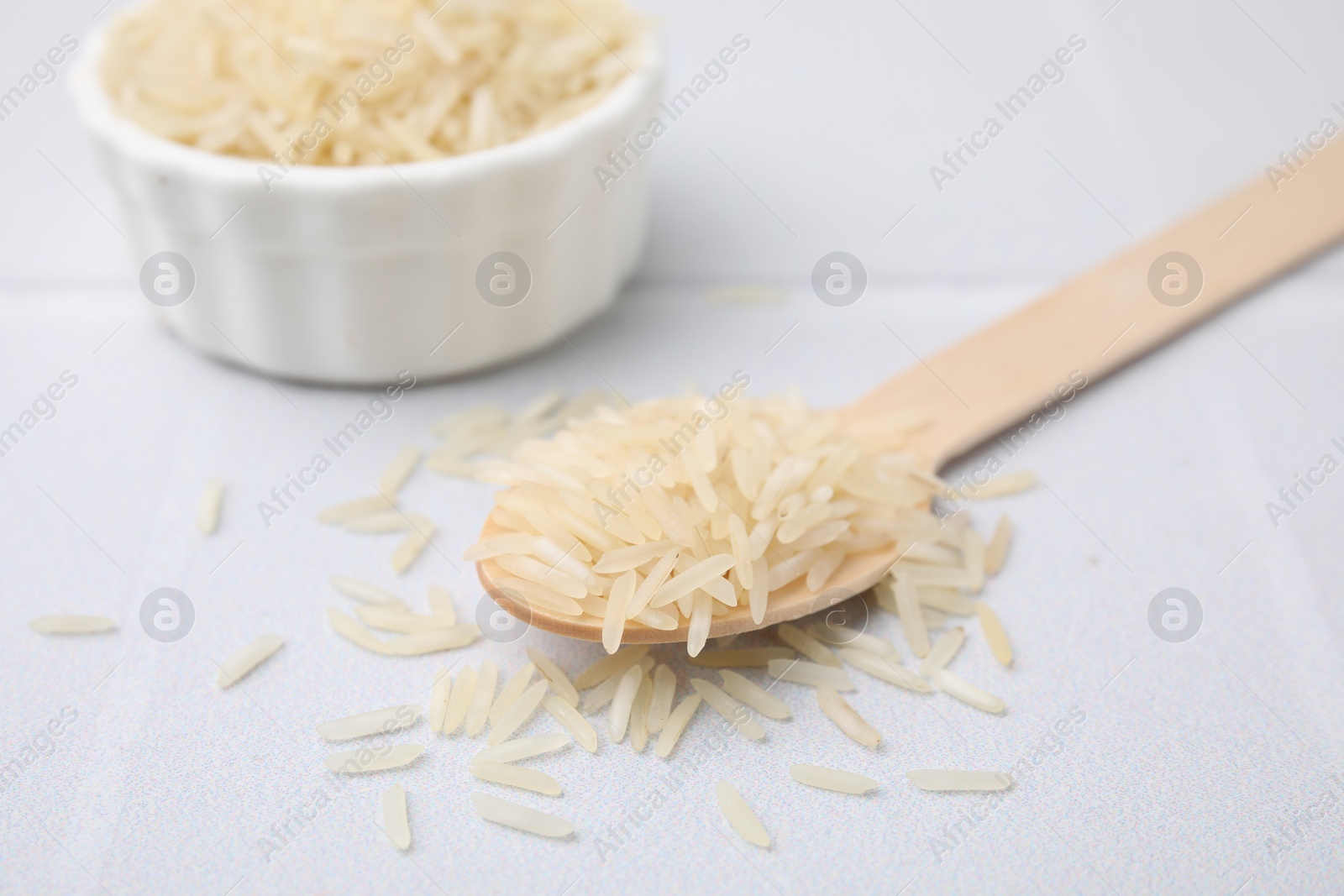 Photo of Wooden spoon and bowl with raw rice on white table, closeup