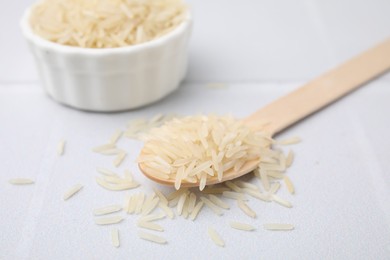 Wooden spoon and bowl with raw rice on white table, closeup