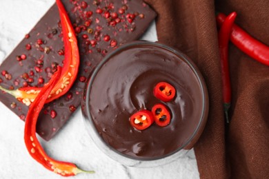 Glass of hot chocolate with chili pepper on white textured table, flat lay