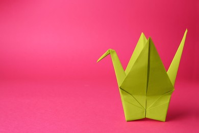 Photo of Origami art. Handmade paper crane on pink background, space for text