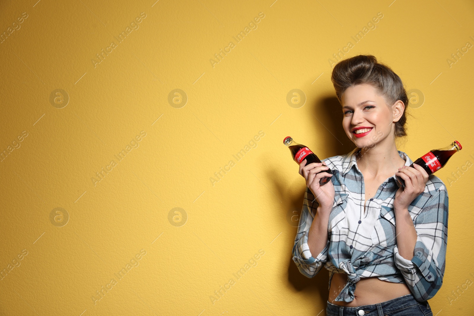 Photo of MYKOLAIV, UKRAINE - NOVEMBER 28, 2018: Young woman with bottles of Coca-Cola on color background, space for text