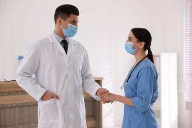 Photo of Doctors with protective masks giving handshake in clinic