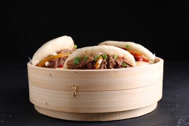Photo of Delicious gua bao in bamboo steamer on black table