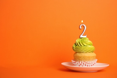 Photo of Birthday cupcake with number two candle in saucer on orange background, space for text