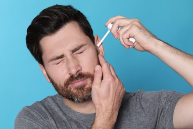 Man using ear spray on light blue background