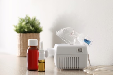Photo of Modern nebulizer with face mask and medications on wooden table indoors. Inhalation equipment