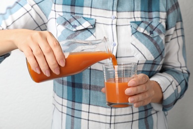 Woman pouring tasty carrot juice from bottle into glass on grey background, closeup