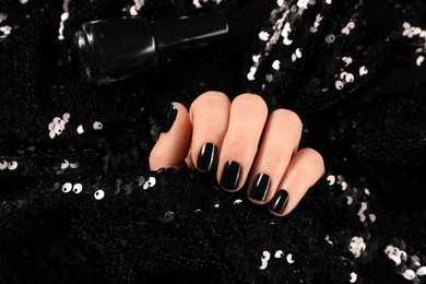 Photo of Woman with black manicure holding shiny fabric, closeup. Nail polish trends