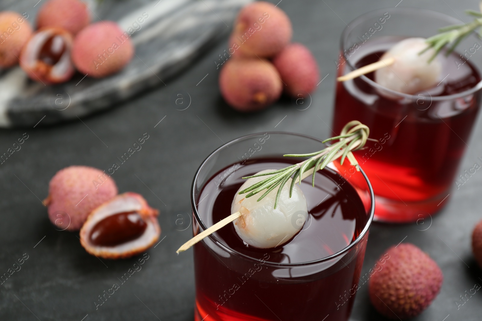 Photo of Glasses of delicious lychee cocktails with rosemary and fresh fruits on black table, closeup