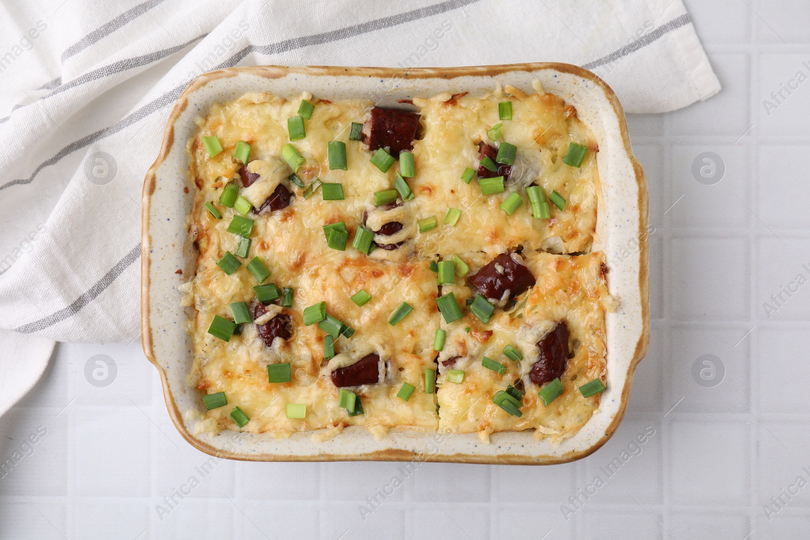 Photo of Tasty sausage casserole in baking dish on white tiled table, top view