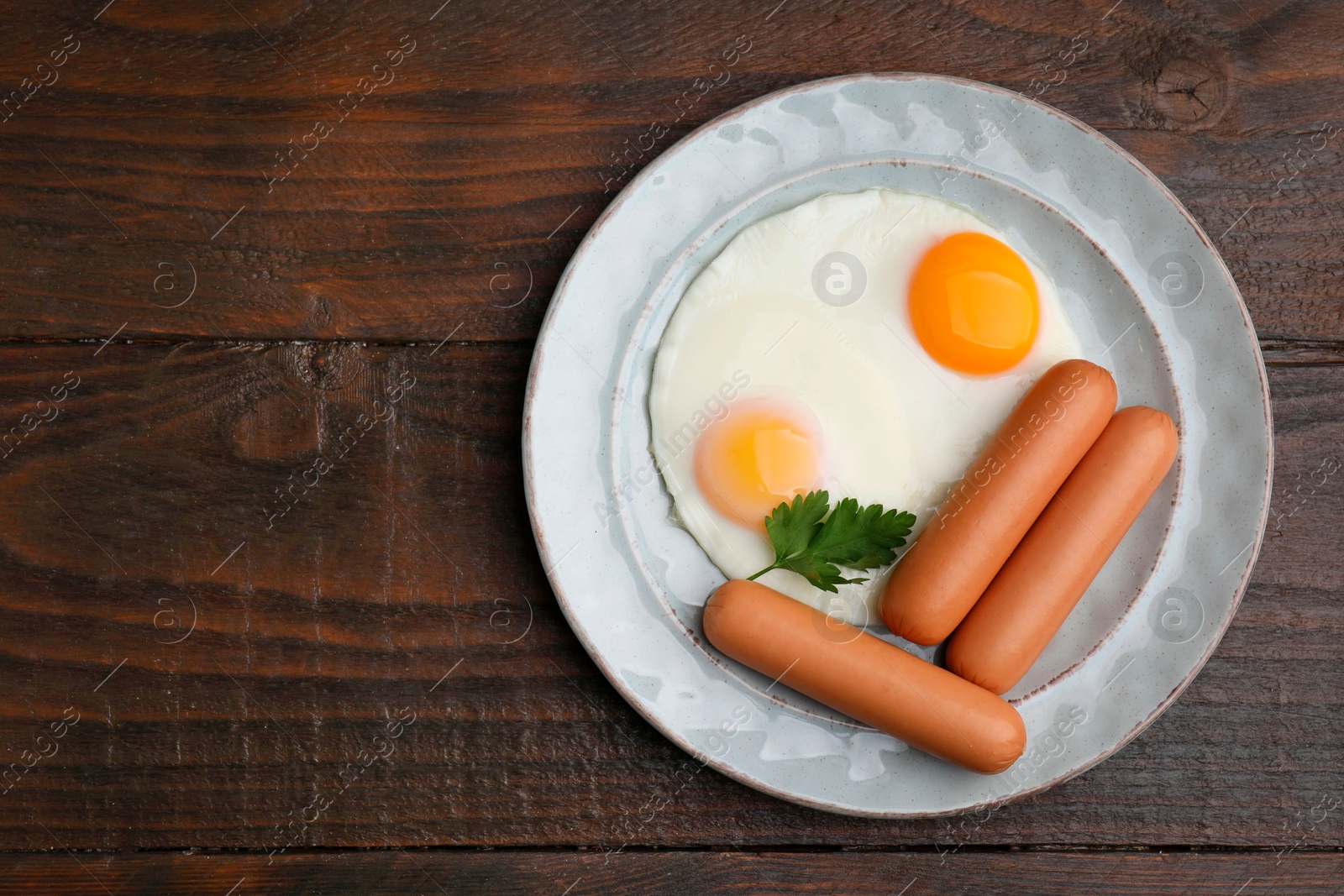 Photo of Delicious boiled sausages, fried eggs and parsley on wooden table, top view. Space for text